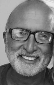 Black and white photo of Andy Rooks smiling, with grey beard and mustache, and black glasses